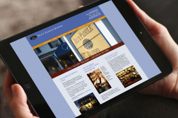 Hands holding iPad displaying Blue Paddle Bistro website