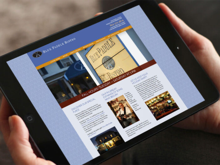 Hands holding iPad displaying Blue Paddle Bistro website