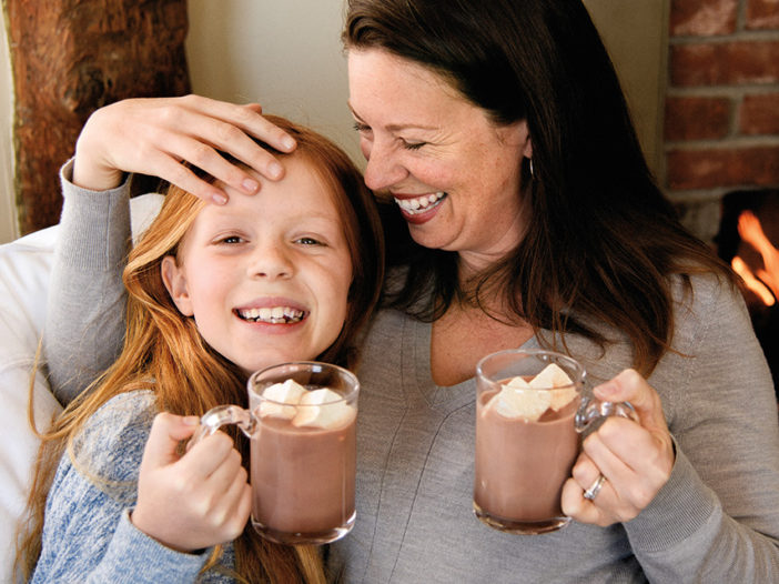 A parent and child smiling while holding hot chocolate