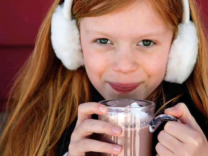 girl drinking hot chocolate with earmuffs on