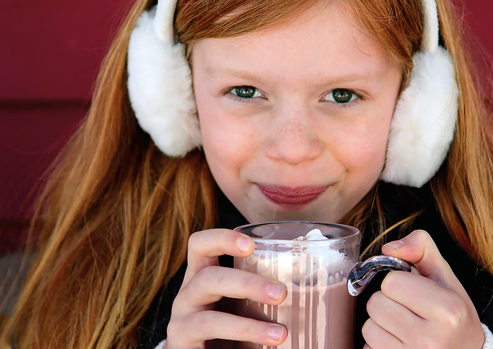 girl drinking hot chocolate with earmuffs on