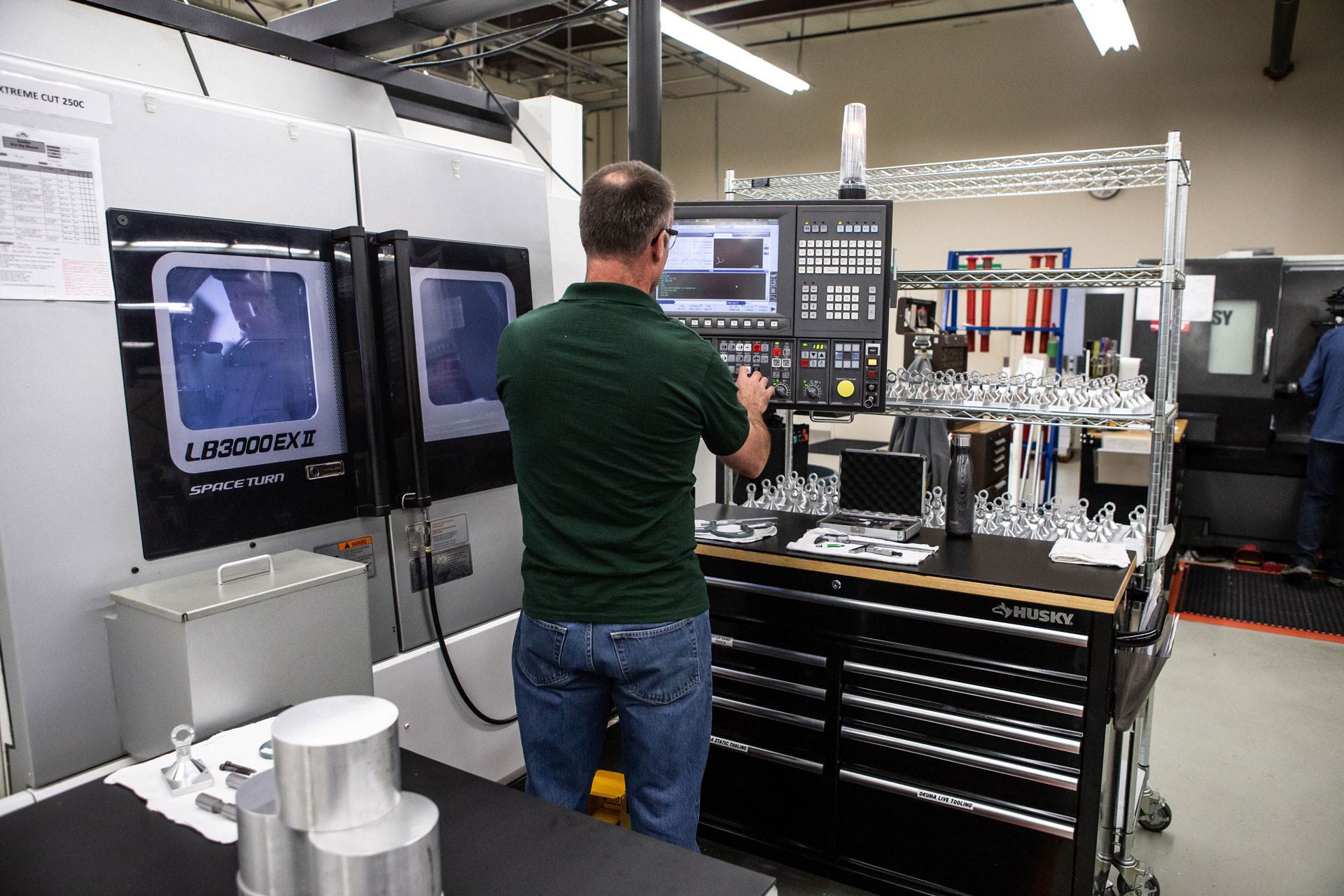 Person standing at controls of CNC machine at Pre-Tech Precision Machining