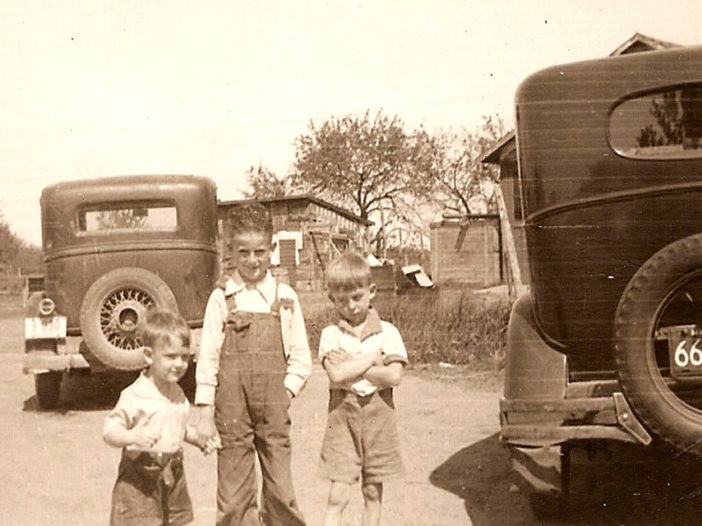 A black and white photograph of three children next to cars