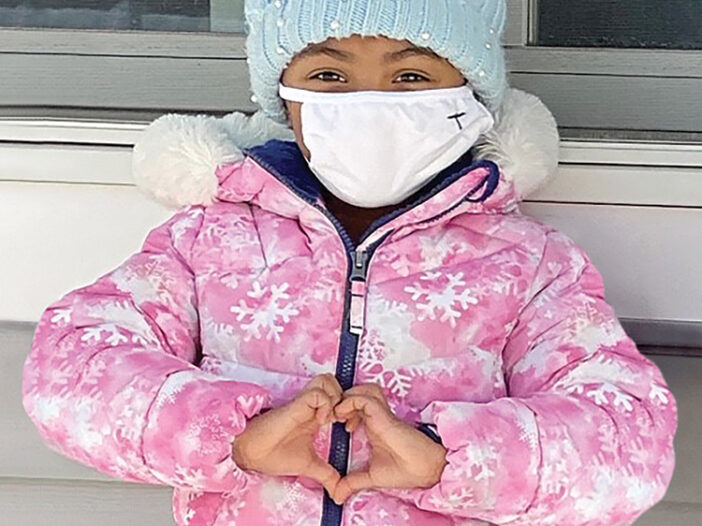 child in winter clothes making a heart sign