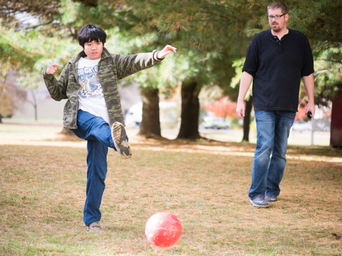 A child kicks a ball with an adult in the background