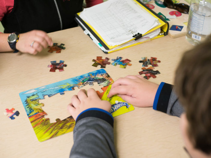 A puzzle is being made on a table, three hands are shown