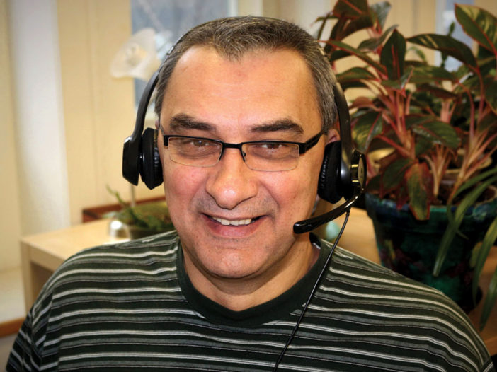 Smiling man with a headset on, looking towards camera.