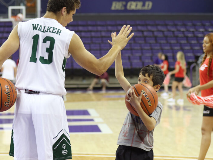 Basketball player giving a high five to a younger child holding a basketball