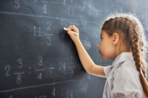 A young girl writing with chalk on a chalkboard