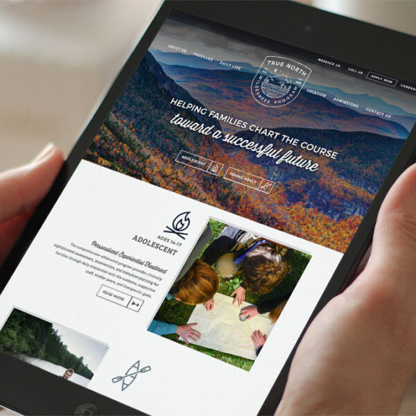 Hands holding iPad displaying True North Wilderness Program website