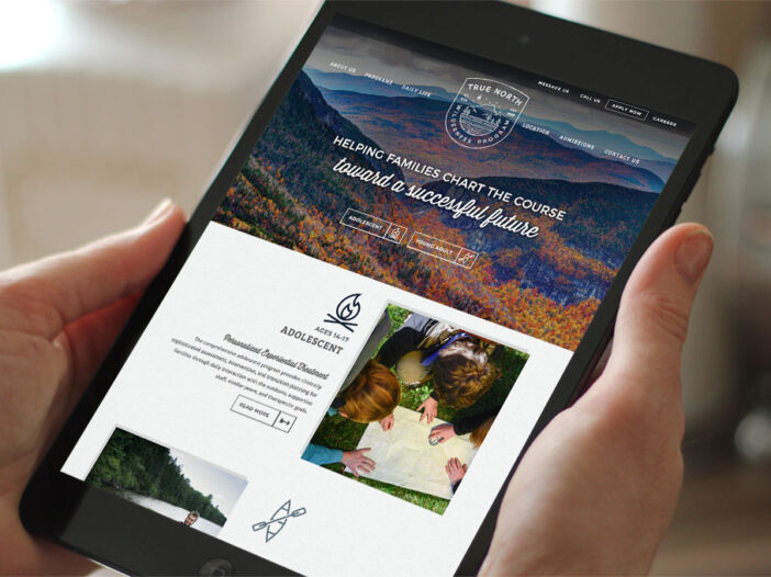 Hands holding iPad displaying True North Wilderness Program website