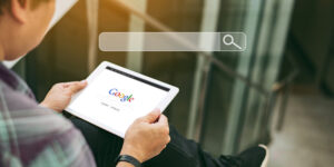 search engine website, person holding a tablet showing Google's website in background